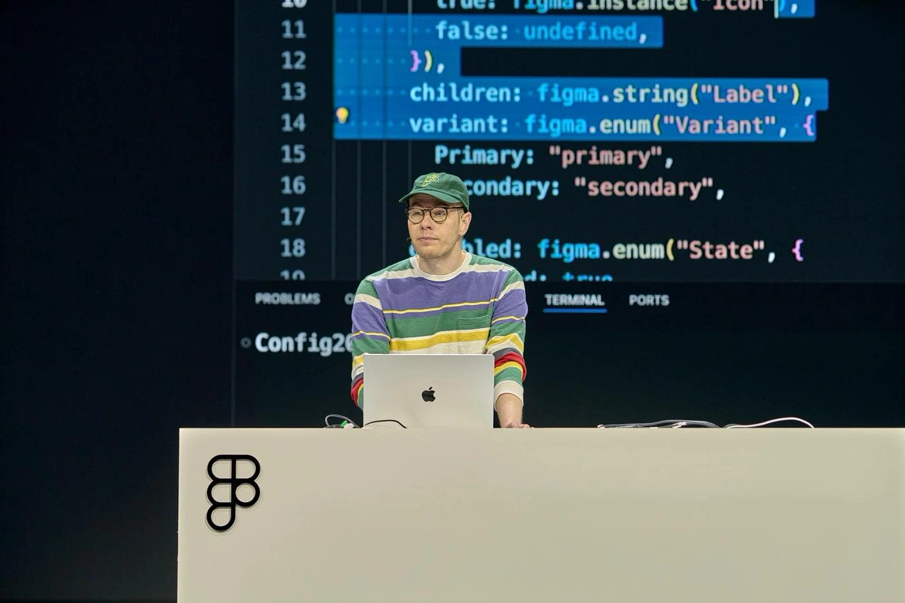 A presenter on the Config 2025 main stage demoing Code Connect, with Figma plugin API code projected on screen behind them