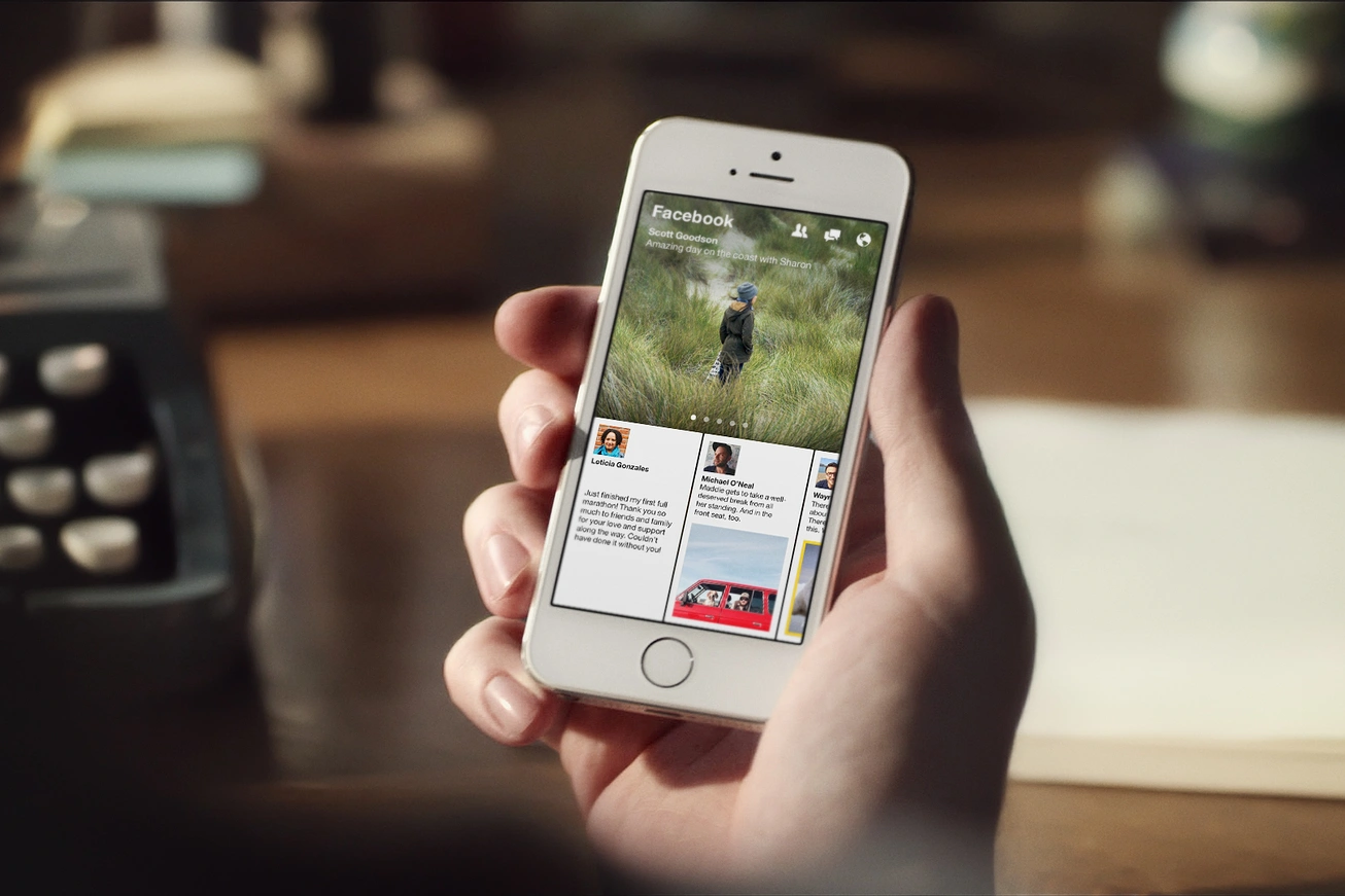 Facebook Paper running on an iPhone — a full-bleed photographic News Feed on a handset held above a desk with a typewriter behind it.