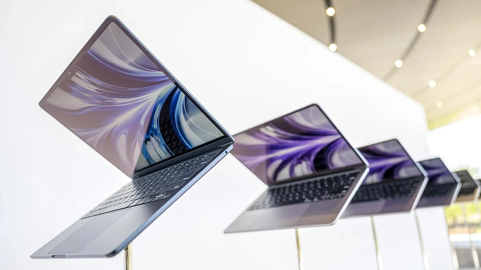A row of thin aluminum MacBook Pros on display, partially open, shot at an angle under warm lighting.