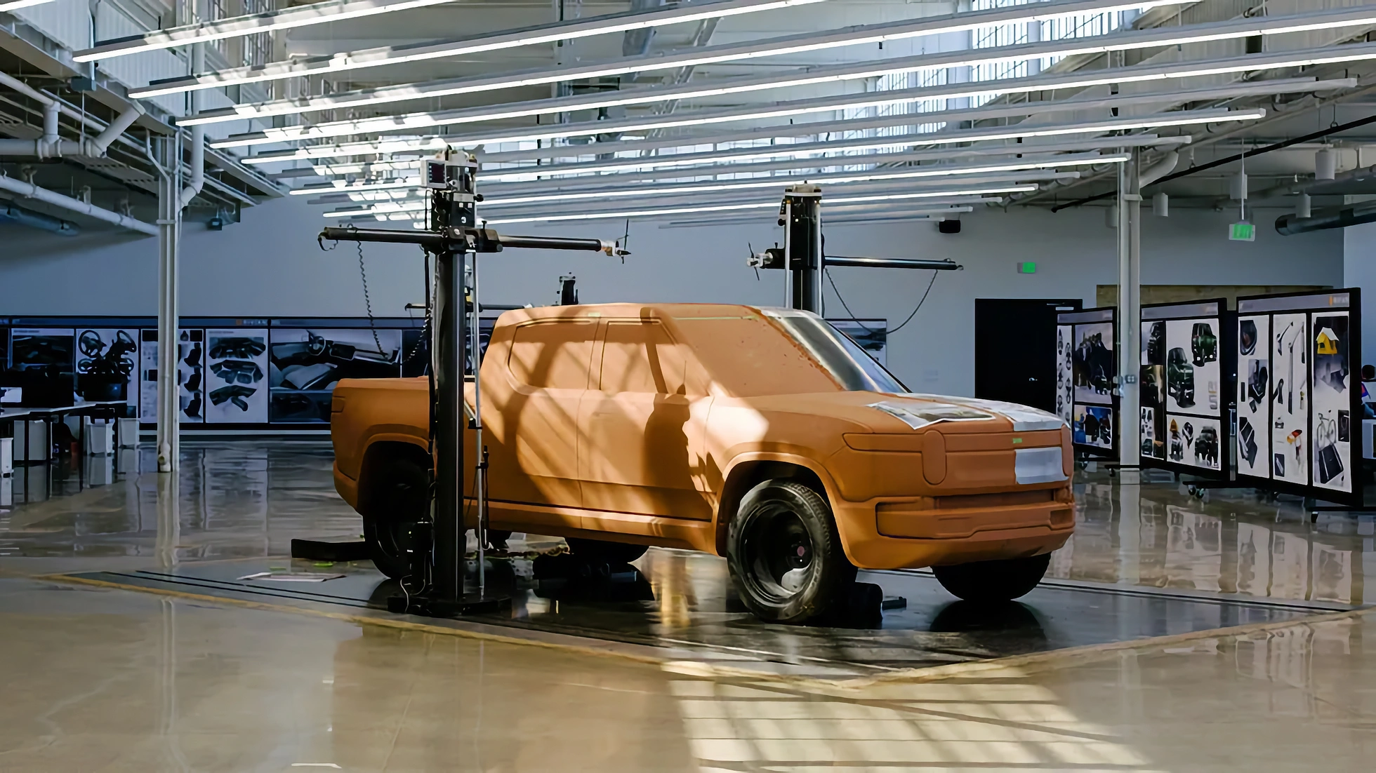 A full-size automotive clay model in a Rivian design studio, sculptors shaping the surface by hand under studio lighting.
